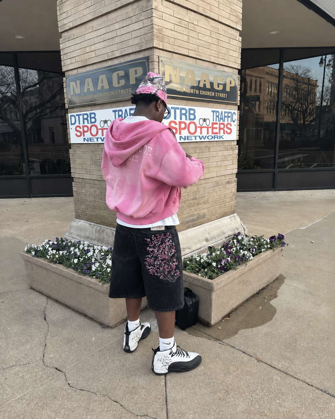 Black sakura jorts worn from the back with a pink hoodie and white sneakers