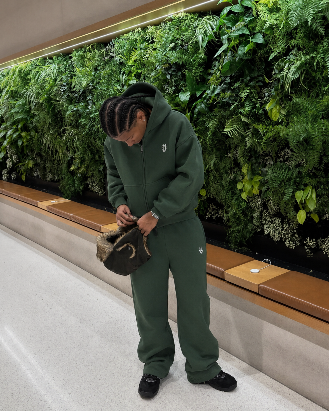 Jogging Essentiel vert baggy porté devant un mur végétal
