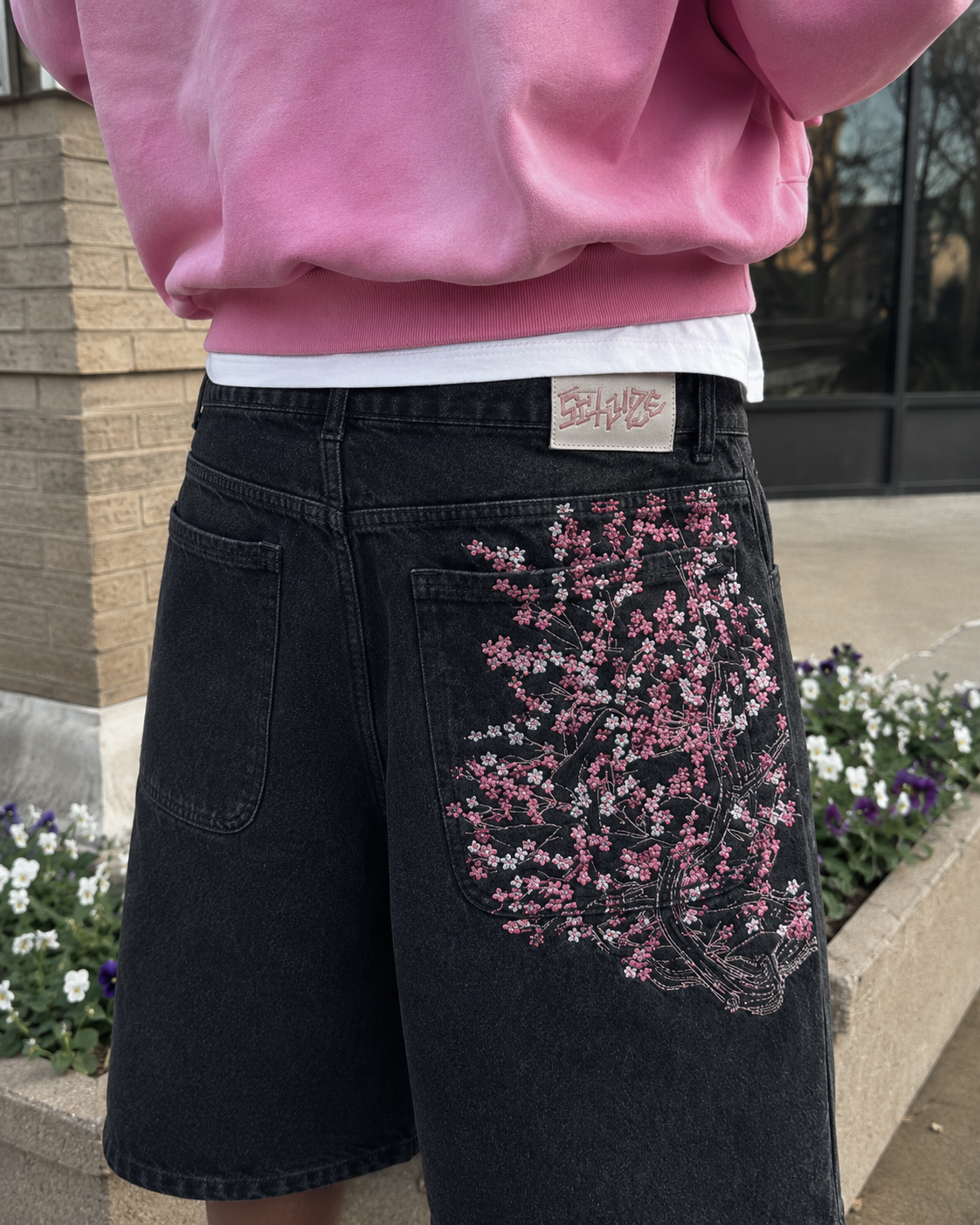 Pink sakura embroidery detail on the back pocket of the black jorts