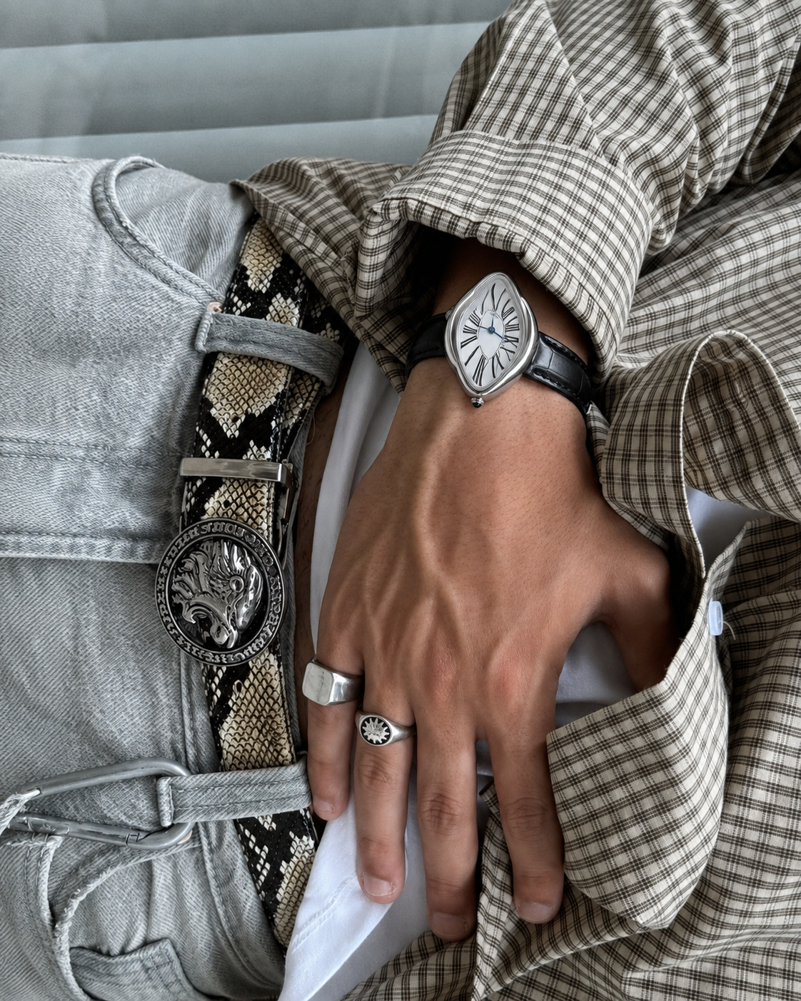 Montre Melting argentée portée avec chemise à carreaux et bagues